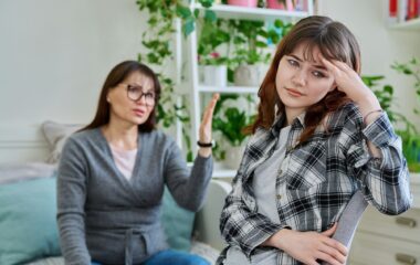 Conflict between mother and teen daughter, offended teenage girl sitting with back