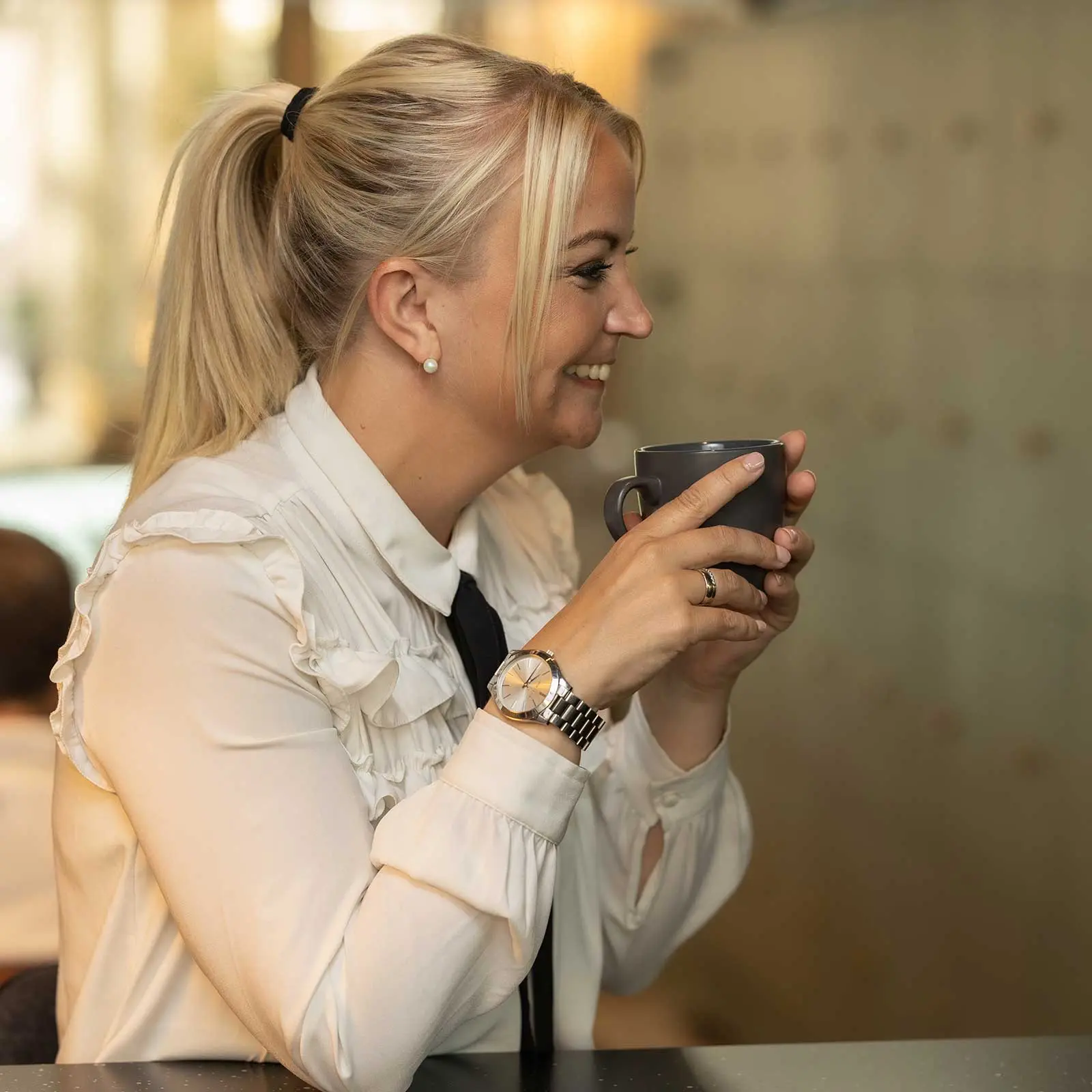 Kvinna sitter med en kaffe kopp i handen och ser glad ut